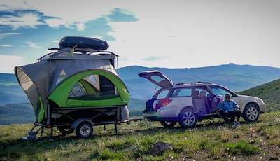 A SylvanSport GO parked on the side of a mountain with the tent pod open and hitched to a vehicle with the trunk open
