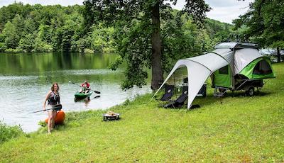 A family kayaking on a lake with their SylvanSport GO parked near the shore with an attached awning