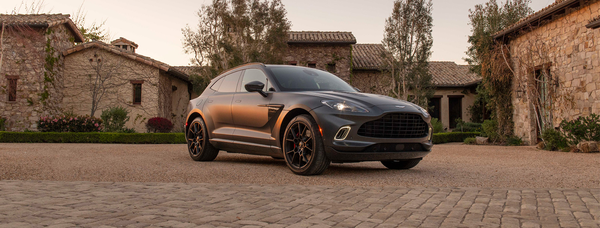 Gray 2021 Aston Martin DBX SUV at golden hour in front of rustic estate
