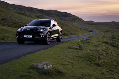 A black 2021 Aston Martin DBX driving down a country road at dusk.