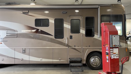 A brown Ford-chassis motorhome parked in the Skaha Ford repair facility, with a red diagnostic tool placed beside it.
