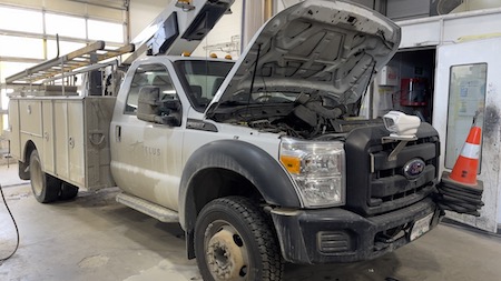 A white Ford fleet truck parked at the Skaha Ford repair facility, with its hood popped open.