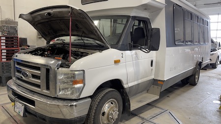 A white Ford motorhome with its hood popped open while parked at the Skaha Ford repair facility.