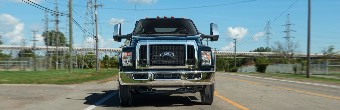 A blue 2022 Ford F-650 driving down a road, with power lines and fencing flanking both sides.