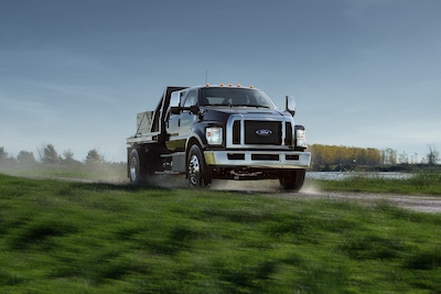 A black 2022 Ford F-650 driving down a country road, with a blue sky in the background and grass flanking both sides of the road.