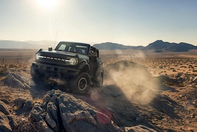 A black 2022 Ford Bronco Badlands SUV driving in a desert environment, with mountains and a blue sky in the background.