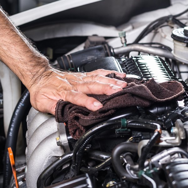 Close-up of a car engine, with a hand using a rag to wipe it down.